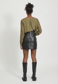 Haut vert olive avec des manches texturées, associé à une mini-jupe en cuir noire dotée d'une fermeture éclair au dos. Bottes noires montantes jusqu'aux genoux.