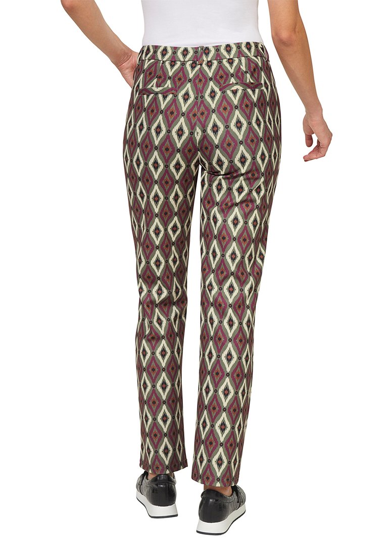 Spodnie slim-fit w wzór z geometrycznym wzorem diamentów w kolorach bordowym, kremowym i czarnym. Widoczne tylne kieszenie; noszone z ciemnymi butami.