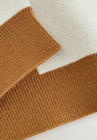 Gestrickter Pullover mit cremefarbenen und braunen Abschnitten. Verfügt über einen strukturierten, gerippten Saum und Ärmelbündchen, die einen Kontrast in Farbe und Muster zeigen.
