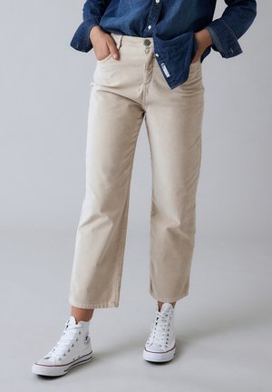 Beige cropped bukser lavet af blød bomuld med et klassisk fem-lomme design og metal knaplukning, parret med hvide høj-top sneakers.