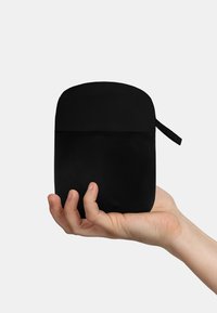 Schwarz zylindrisches Täschchen, das in einer Hand gehalten wird, mit einer glatten Stoffoberfläche und einem Reißverschluss oben. Enthält eine seitliche Schlaufe zur Befestigung.