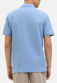 Himmelblaues Poloshirt aus strukturiertem Stoff, mit kurzen Ärmeln und klassischem Kragen. Es hat eine entspannte Passform und Schlitze an dem Saum.