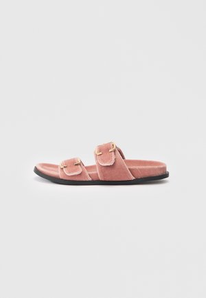 Sandale rose en velours à enfiler avec deux courroies réglables en or et semelle plate noire sur fond blanc.