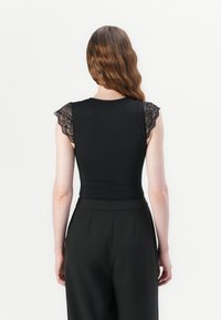 Black bodysuit with lace cap sleeves, fitted torso, and smooth texture. Paired with high-waisted black trousers. Simple, elegant design.