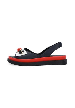 Czarna i czerwona sandałka typu slingback z białą i czerwoną ozdobną klamrą na przednim pasku oraz grubą czarną podeszwą.