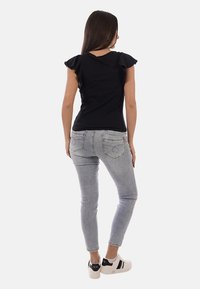 Donna in piedi di spalle che indossa una maglietta nera con maniche a volant, jeans skinny grigio chiaro e sneakers bianche con dettagli neri.