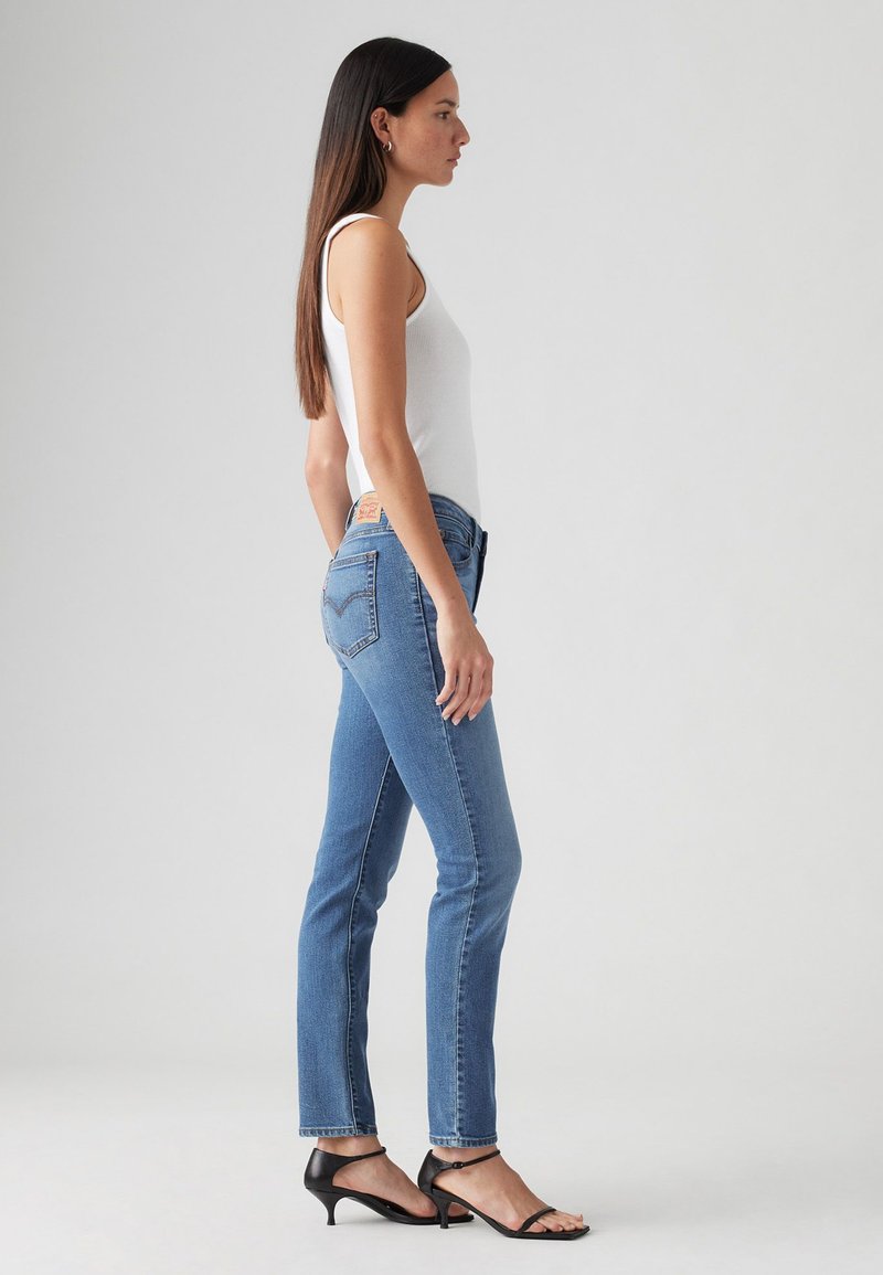 Jeans ajustados de mezclilla azul con un lavado claro. Presenta cinco bolsillos, trabillas para el cinturón y una etiqueta de Levi's descolorida en la cinturilla.