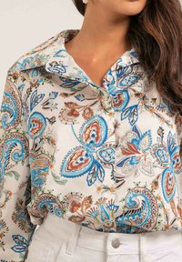 Chemise à boutons florale en tissu léger, ornée d'un motif paisley vibrant avec des accents bleus, marron et orange. Détails du col et des poignets visibles.
