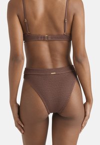 Set bikini marrone con texture, caratterizzato da una parte posteriore arricciata, spalline regolabili e dettagli in metallo dorato sulla parte superiore e inferiore.