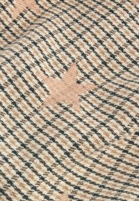 Textiel met een geweven houndstooth patroon in zwart, beige en wit, met roze sterren als opvallende ontwerpelementen. Zachte textuur.