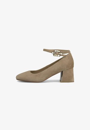 Chaussure à talon haute en suède beige avec un bout pointu, une sangle de cheville ornée d'un accent en cristal, et un talon carré avec un détail métallique.