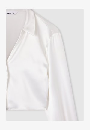 Camicia corta in satin bianco con collo a camicia, maniche lunghe e texture liscia. Presenta un design pulito e una vestibilità su misura.