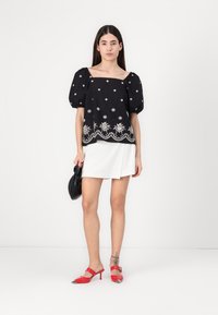 Top nero a maniche puff con ricamo bianco, scollatura quadrata, orlo decorativo, abbinato a una mini gonna bianca e scarpe con tacco rosso.