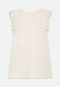 Top bej deschis fără mâneci, cu detalii volanate pe umeri, gât rotund și croială lejeră. Confecționat din material moale de bumbac.