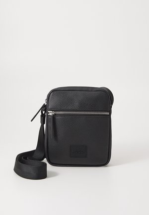 Sort læder crossbody taske med en tekstureret overflade, der har en lynlåslomme foran, justerbar strop og et logo-label på forsiden.