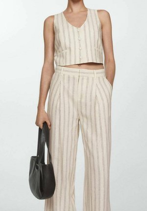 Top corto beige sin mangas y pantalones de pierna ancha de talle alto con rayas verticales, persona sosteniendo un bolso negro de cuero en la mano izquierda.