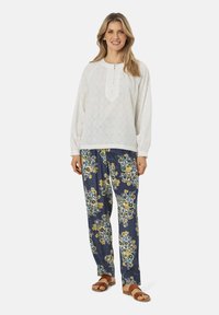 Hvid langærmet bluse med knapdetaljer og tekstureret stof, parret med marineblå bukser med blomstermønster i gul og blå, båret med brune sandaler.