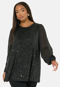 Svart paljett-topp med långa genomskinliga puffärmar, rund halslinning och rak skärning. Den glansiga ytan har olika reflekterande paljetter.