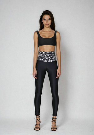 Top cropped nero abbinato a leggings a vita alta con una stampa leopardata bianca e nera. La modella indossa tacchi neri con fasce.