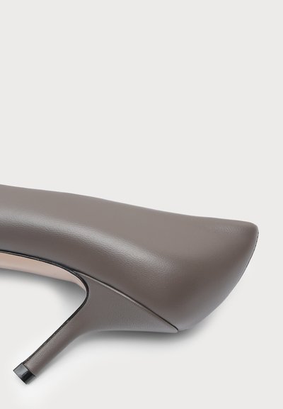 Gros plan d'une chaussure à talon haut en cuir taupe à bout pointu avec un talon stiletto fin et de hauteur moyenne sur fond blanc.