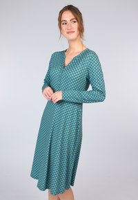 Grünes, langärmliges Kleid mit V-Ausschnitt, geometrischem Muster und fließendem Rock. Hergestellt aus weichem, strukturiertem Stoff.