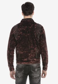 Schwarze und rote Jeansjacke mit Nieten auf den Schultern, distressed Struktur und gesticktem Logo auf dem Rücken. Verfügt über Reißverschlusstaschen.