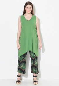 Top sin mangas verde con diseño de escote en V, combinado con pantalones recortados negros que presentan un patrón de hojas de palma verdes y acentos marrones. Sandalias negras.