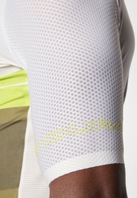 Maglia da ciclismo bianca in rete con design aderente, dettagli verdi e tessuto testurizzato. Logo "INDURAIN" in giallo brillante vicino all'orlo.