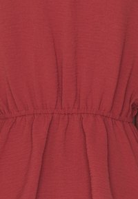 Tissu rouge avec une finition texturée, présentant un élastique froncé à la taille qui crée une silhouette fluide. Pas de motifs ou d'accents visibles.