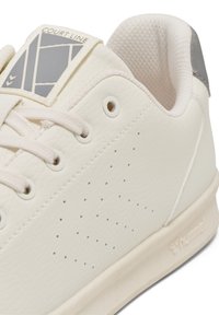 White synthetic leather sneaker with textured surface, minimal perforations, white laces, logo patch, and light gray accent on the heel.