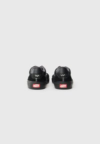 Black sneakers with a suede upper, gray accents, and a textured back panel. Features a logo and red "Off the Wall" tag on the sole.