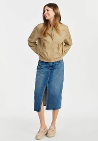 Jasnobrązowa kurtka bombowca z zamkami, w połączeniu z dżinsową spódnicą midi z przednim rozcięciem. Jasne, grube buty typu slip-on.