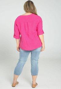 Chemise en lin rose avec manches retroussées, ourlet arrondi, associée à un jean court bleu clair. Le mannequin porte des chaussures plates beige.