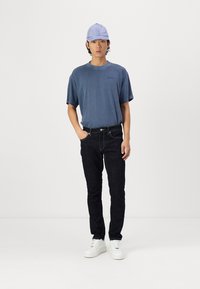 Light blue short-sleeve t-shirt with round neck, dark denim skinny jeans, and white sneakers. A light purple cap completes the outfit.