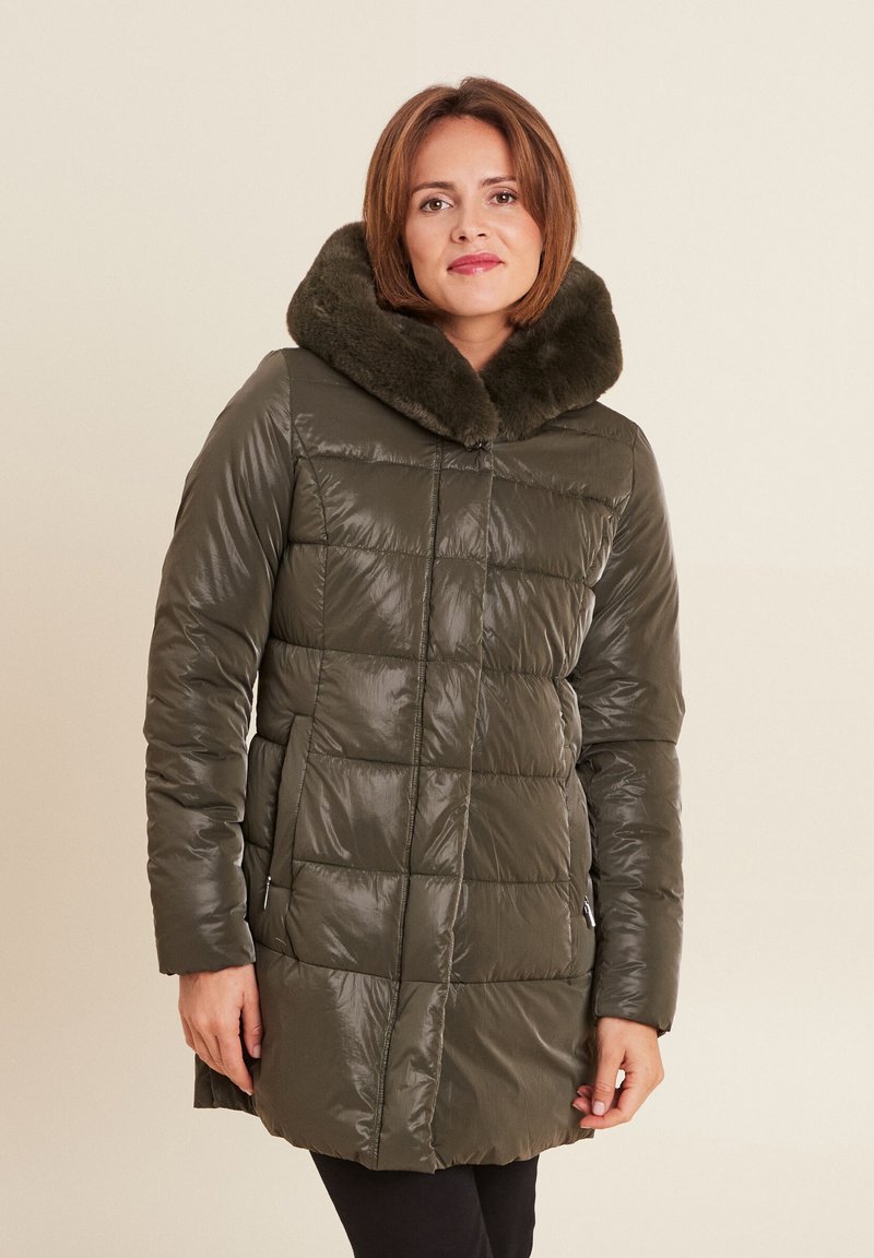 Gevoerde groene jas met een nepbont kraag, voorzien van een doorgestikt patroon, ritszakken en een glanzende afwerking. Lange mouwen en een knielange snit.