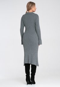 Szara dzianinowa sukienka w prążki z długimi rękawami i dopasowanym krojem. Posiada okrągły dekolt oraz wysoki rozcięcie z tyłu. Czarne kozaki do kolan.