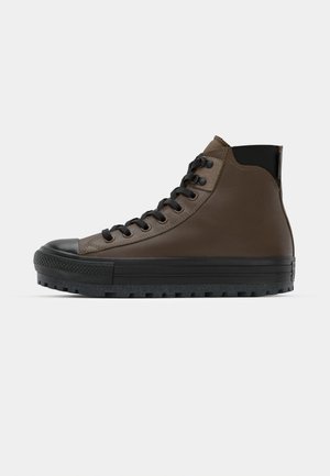 Brown high-top sneaker with a smooth leather upper, black rubber toe cap, and textured black sole. Features black laces and eyelets.