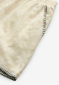 Kratke hlače od pamučne tkanine u boji slonovače s uzorkom palmovih listova i elastičnom waistbandom, te crnim šavovima duž ruba.