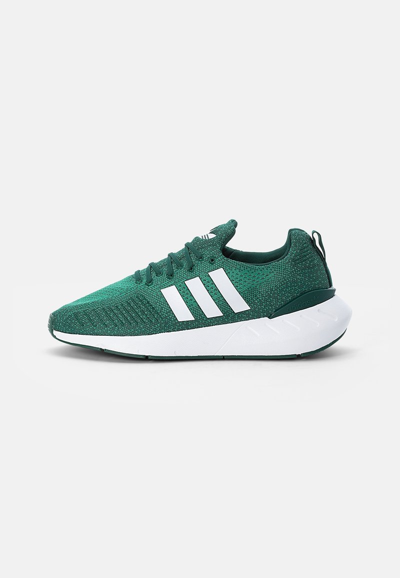 Baskets de sport vertes en tricot avec trois bandes blanches et semelle épaisse blanche, vues de profil sur un fond uni.