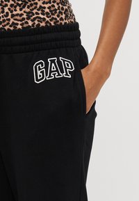 Melni sporta bikses ar elastīgu jostasvīru un sānu kabatām, ar balto "GAP" logotipa izšuvumu kreisajā kājā.