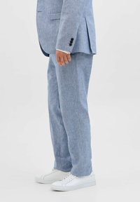 Costum din in de culoare albastru deschis, cu o croială ajustată, având o jachetă cu un singur rând de nasturi și pantaloni drepti, asortați cu adidași albi.