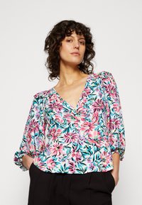 Blusa floral em tecido leve com padrões em rosa, azul e verde. Apresenta um decote em V, mangas bufantes e uma cintura franzida.