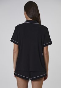 Sort kortærmet top med krave og hvid piping langs ærmerne. Parret med sorte shorts med en lignende hvid detalje.