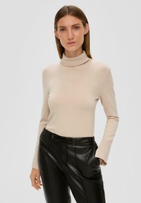 Beige Rollkragenpullover mit langen Ärmeln, enganliegendem Design und glatter Textur, kombiniert mit schwarzen Lederhosen in hoher Taille.