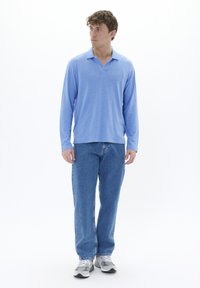 Light blue long-sleeve polo shirt with a V-neck collar, paired with light blue denim jeans and gray athletic shoes.