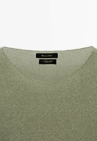 Olivgrüner, gestrickter Pullover mit einem V-Ausschnitt-Design. Das Materialetikett weist auf eine Mischung aus Baumwolle und Leinen hin, hergestellt in Italien. Feine Textur, leicht.