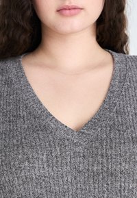 Top tricotat gri cu decolteu în V și textură ribbed. Prezentă un material combinat pentru confort, cu o siluetă ajustată.