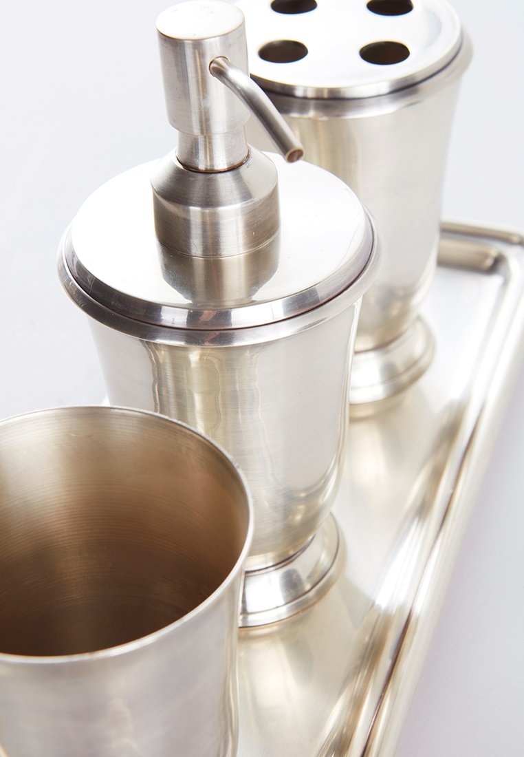 Set av barware i rostfritt stål på en bricka, som innehåller en shaker, en jigger med hål och en kopp. Slät, glänsande yta med rundade former.