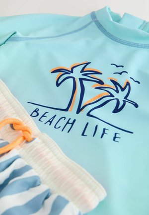 Lyseblå rashguard med palmetrædesign og teksten "BEACH LIFE", kombineret med stribede badetrusser med orange snøre.