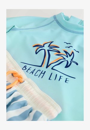 Svetlo modra termo majica z motivom palme in napisom "BEACH LIFE", kombinirana s kopalnimi hlačami z motivom črt in oranžnim vrvico za zategovanje.
